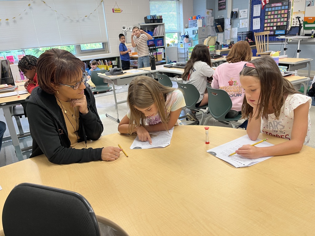 Students work in pairs and take turns reading an article aloud. A teacher works on literacy skills with two students. 