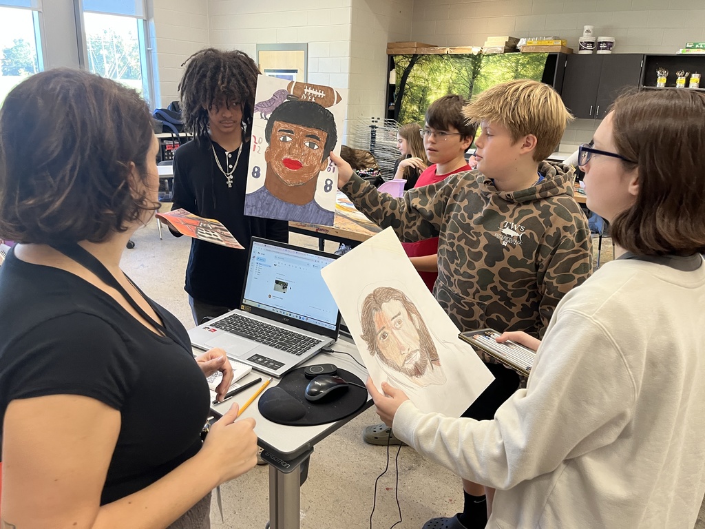 Students show their art teacher portraits they are creating.