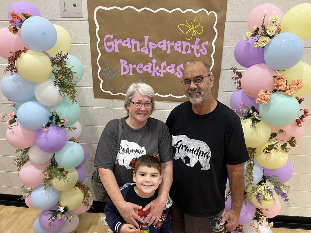 Two adults and one child  pose for a photo at a grandparents breakfast. 