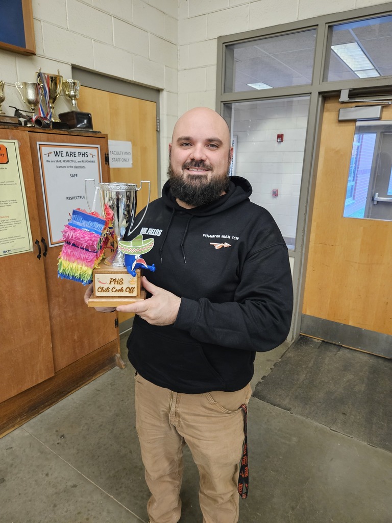 A man poses for a photo while holding a chili cook-off trophy and a small pinata.