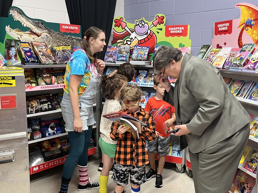 Students search through merchandise at a school book fair.  Adults help.
