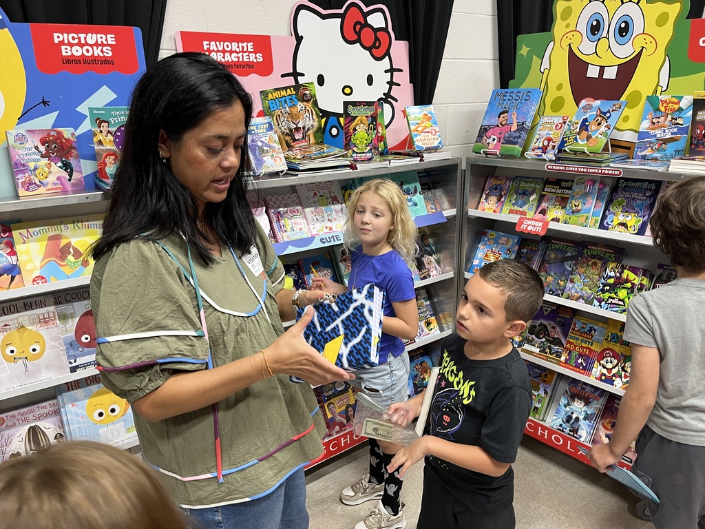 Students search through merchandise at a school book fair.  An adult helps.