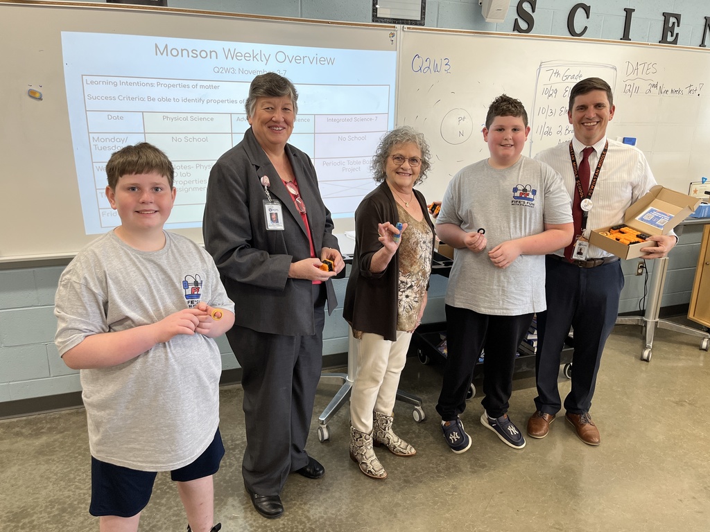 Three adults and two students pose for a photo during a fidget spinner donation.