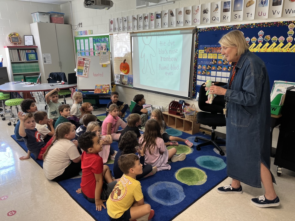 A teacher explains an assignment to students sitting on the floor. 