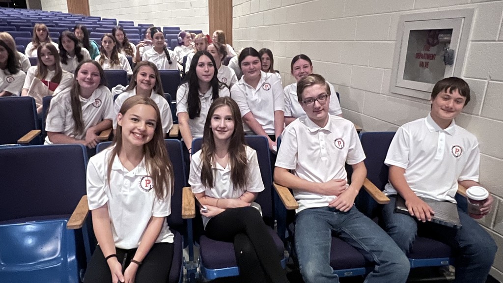 A group of students in matching shirts sit together in an auditorium.