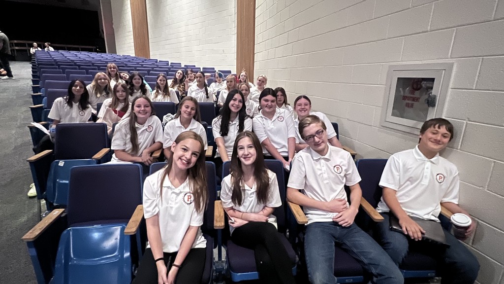 A group of students in matching shirts sit together in an auditorium.