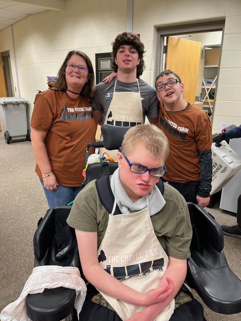 An adult and three students pose for a photo along with a coffee cart.