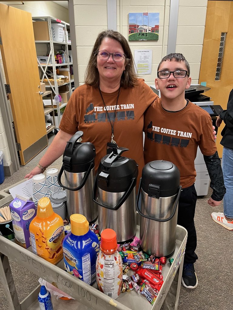 An adult and student pose for a photo along with a coffee cart.