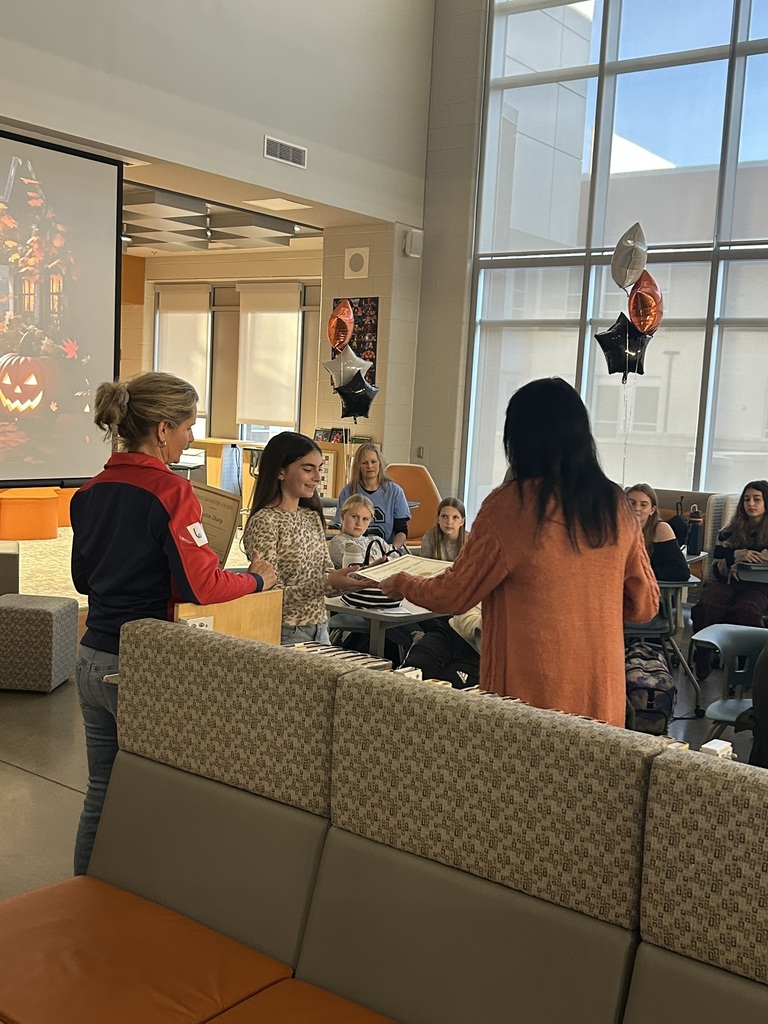 A student accepts a student of the quarter award in an informal ceremony in a library. 