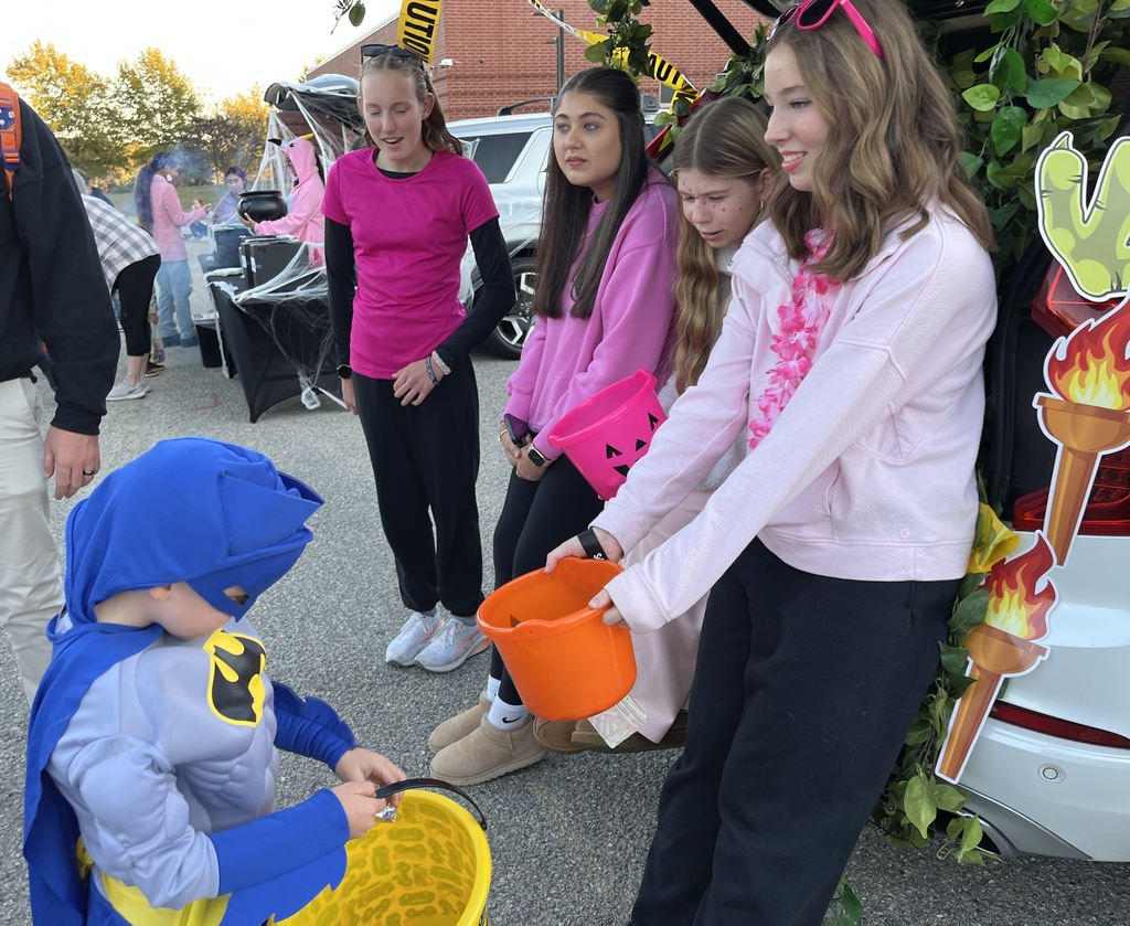 A group of teens give candy to a child in costume.