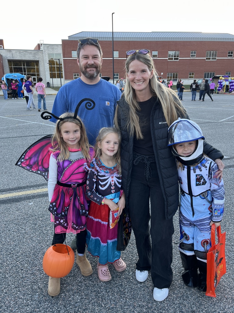 Two adults and three children pose for a photo at a trunk or treat event.