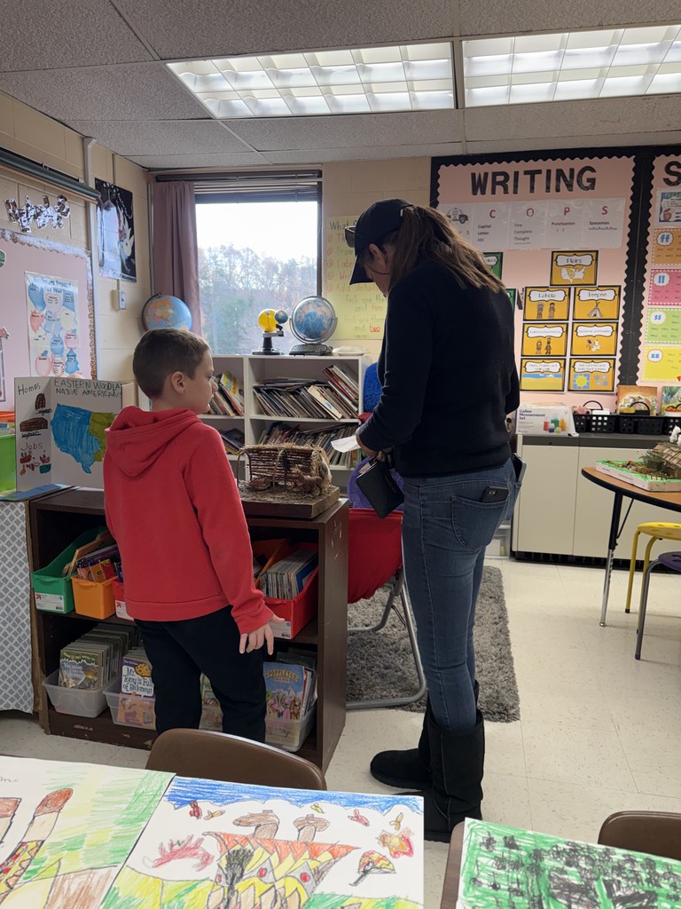 An adult and child observe work on display for a class's Native American Museum.