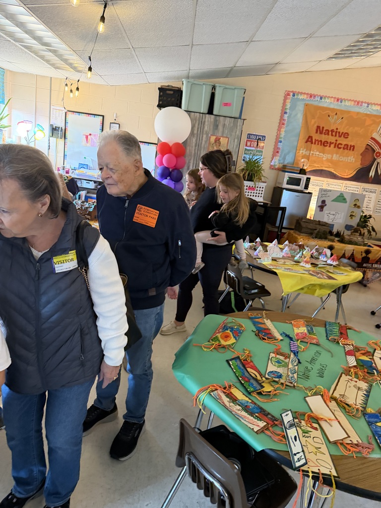 Adults and children observe work on display for a class's Native American Museum.