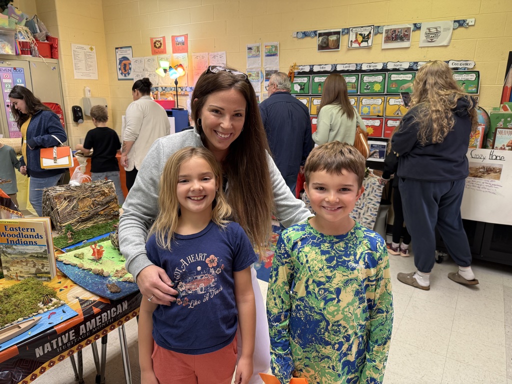 Adults and children observe work on display for a class's Native American Museum.