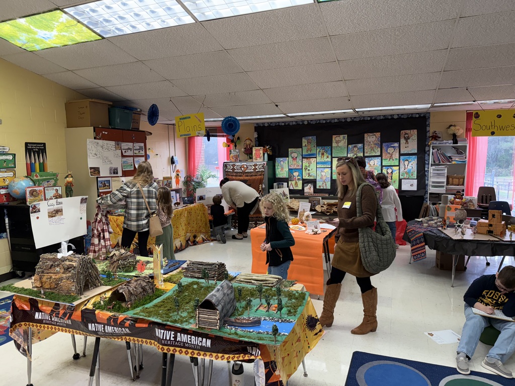 Adults and children observe work on display for a class's Native American Museum.