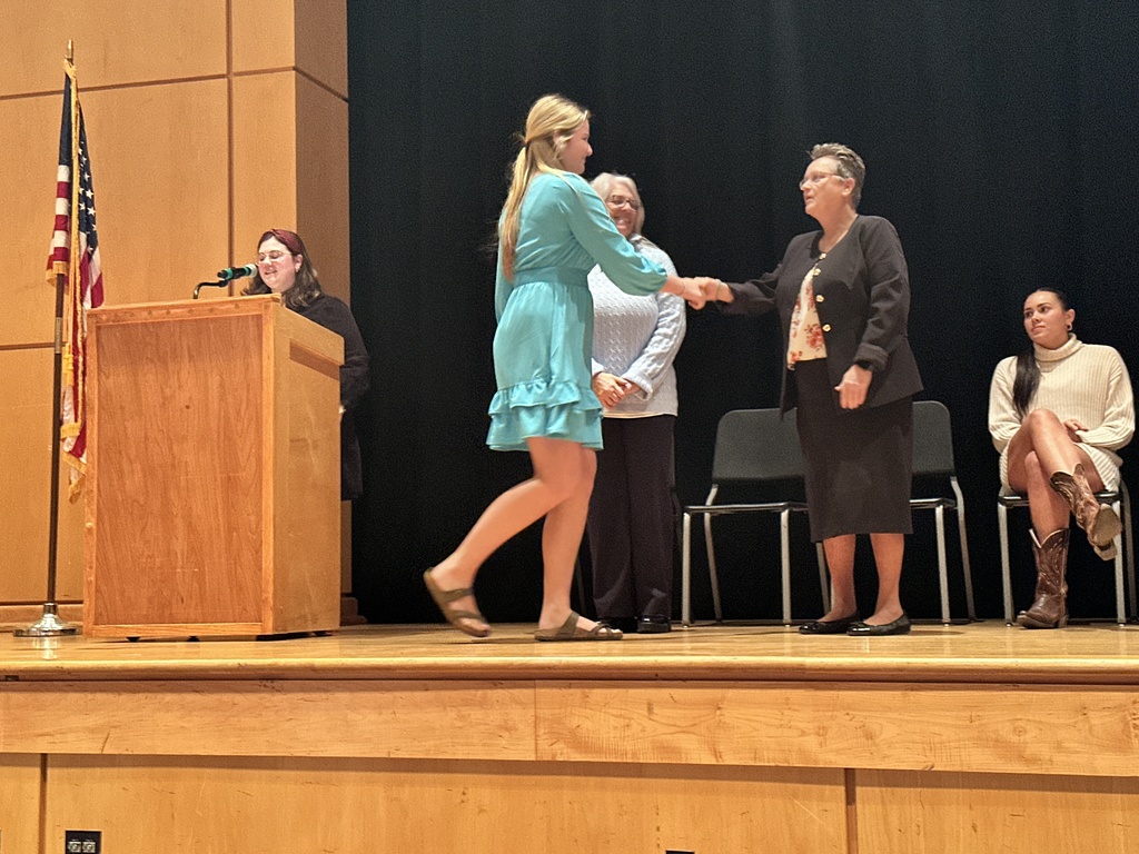 Adults  welcome an inductee during  a National Technical Honor Society induction ceremony.