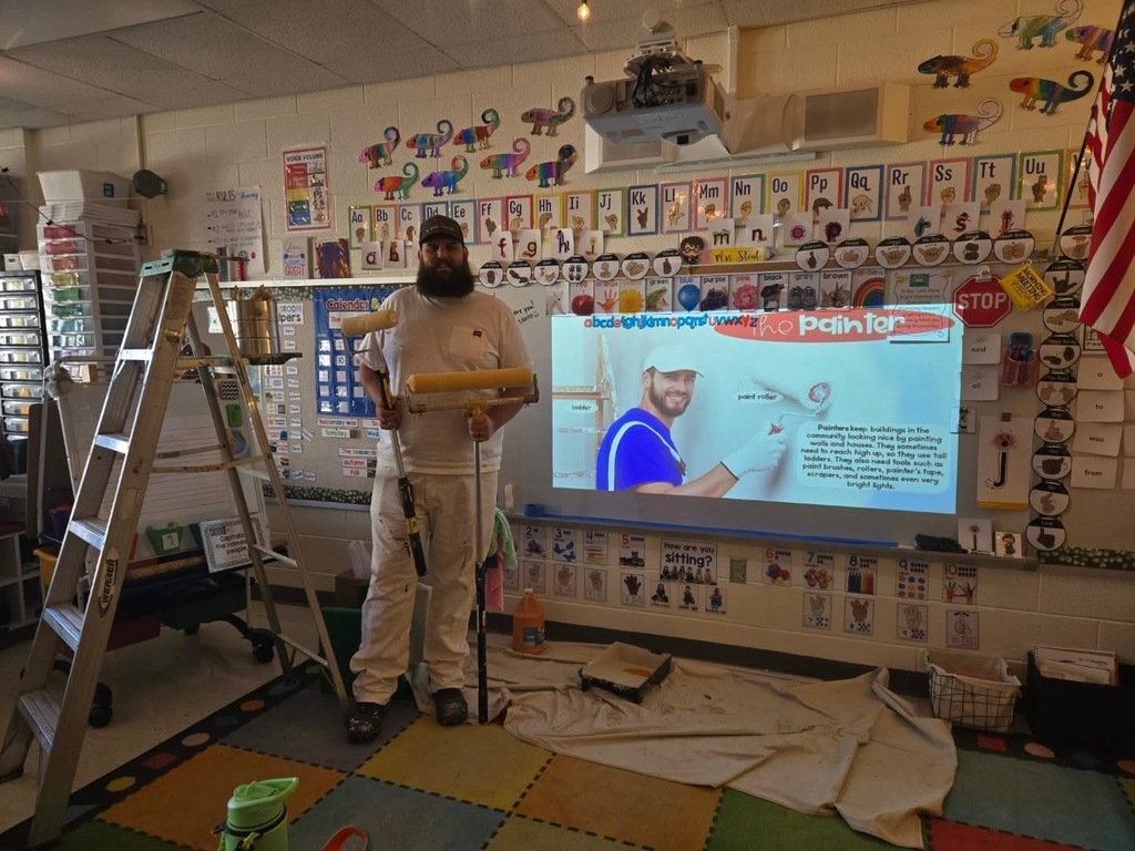 A painter who has come to talk to kindergarteners about painting poses with the tools of his trade. 
