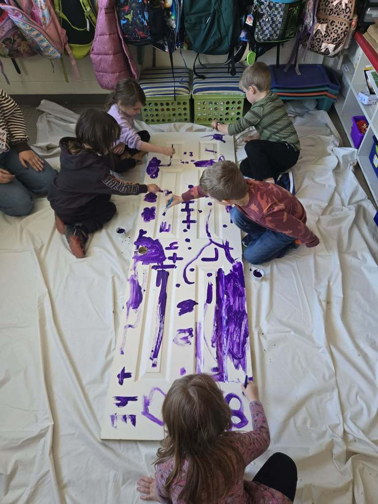 An adult and students paint a pantry door in class. 