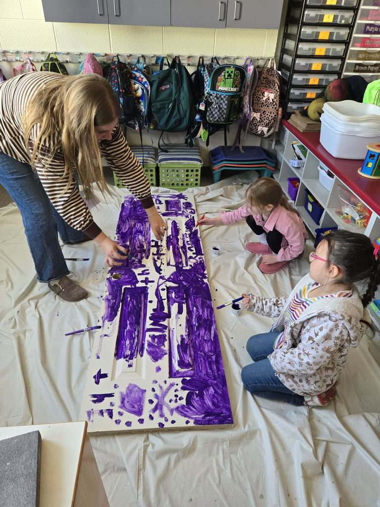 An adult and students paint a pantry door in class. 