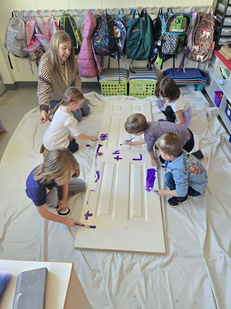 An adult and students paint a pantry door in class. 
