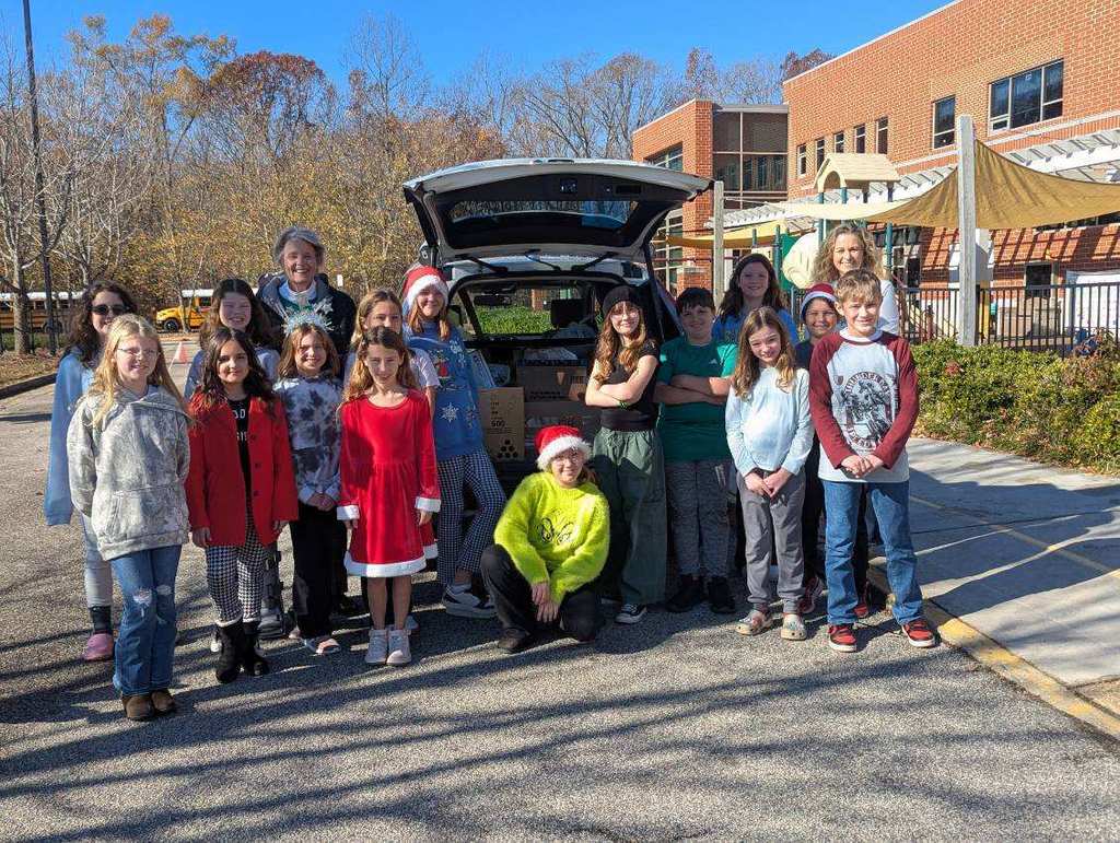 Two women and a group of students pose together in front of a loaded car.