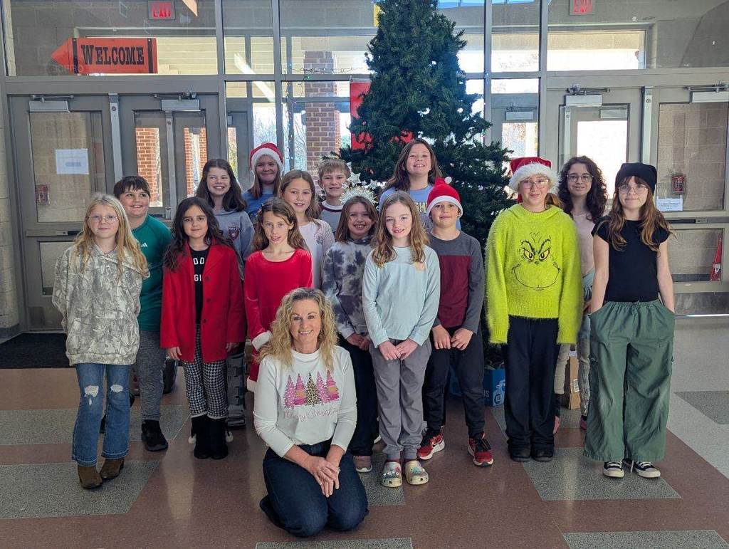 A woman and a group of students pose together in front of a Christmas tree.