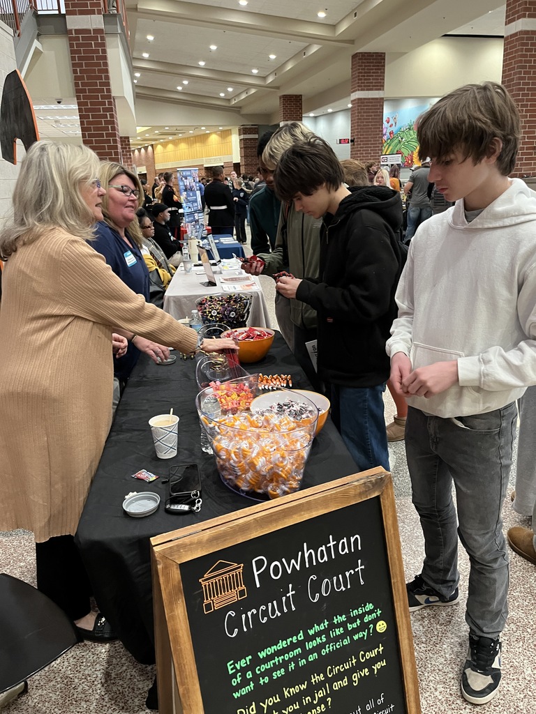 Adults at an information booth at a high school college and career fair speak to students.