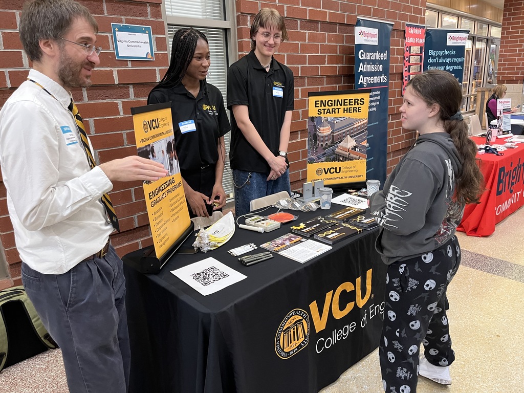 An adult at an information booth at a high school college and career fair speak to a student.