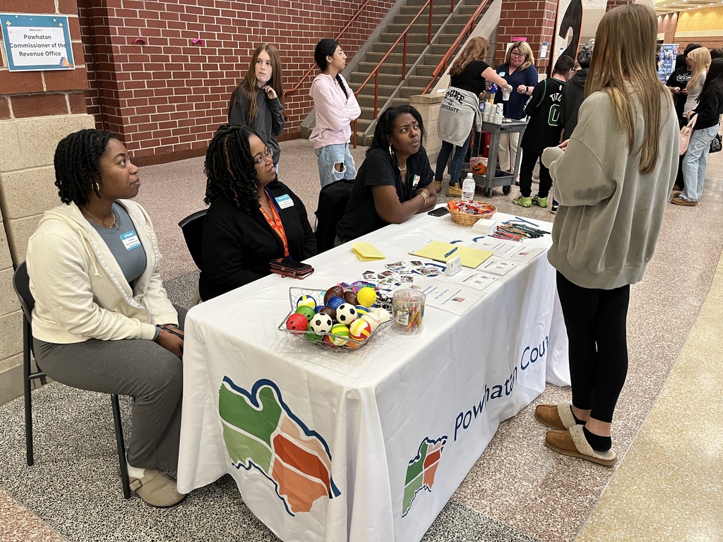 Adults at an information booth at a high school college and career fair speak to a student.