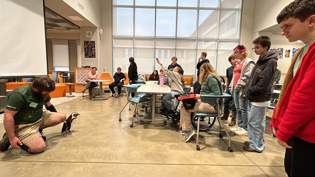 A zookeeper shows a penguin to a  group of students and adults.