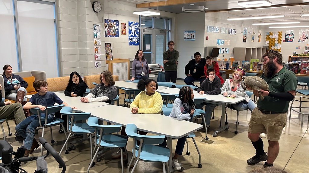A zookeeper shows a tortoise to a  group of students and adults.