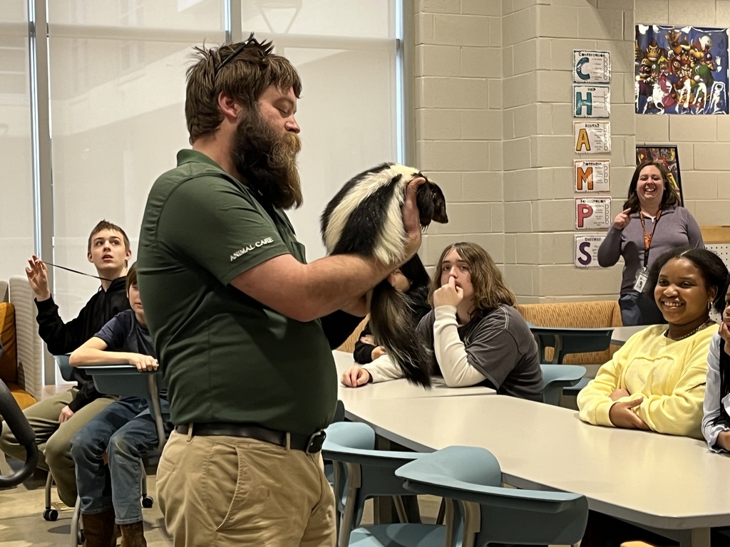 A zookeeper shows a skunk to a  group of students and adults.