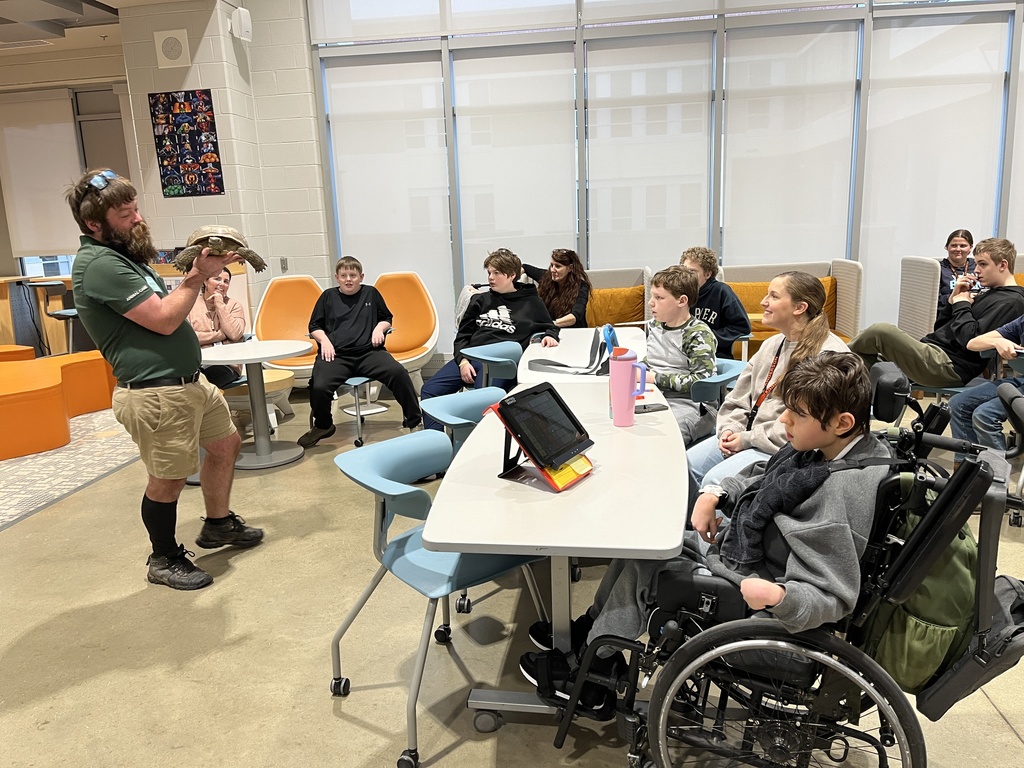 A zookeeper shows a tortoise to a  group of students and adults.