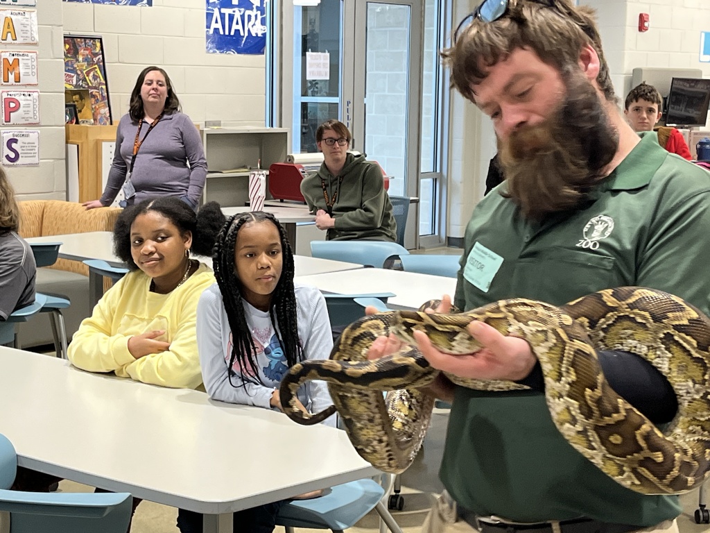 A zookeeper shows a python to a  group of students and adults.
