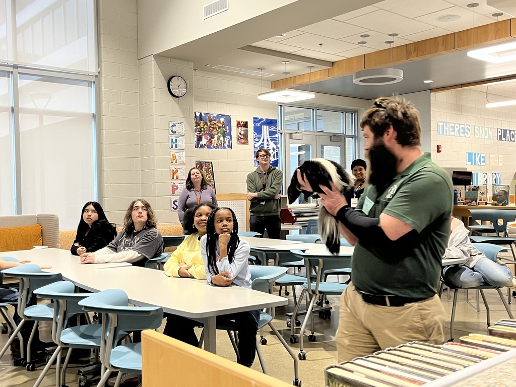 A zookeeper shows a skunk to a  group of students and adults.