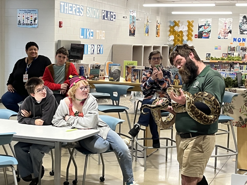 A zookeeper shows a python to a  group of students and adults.