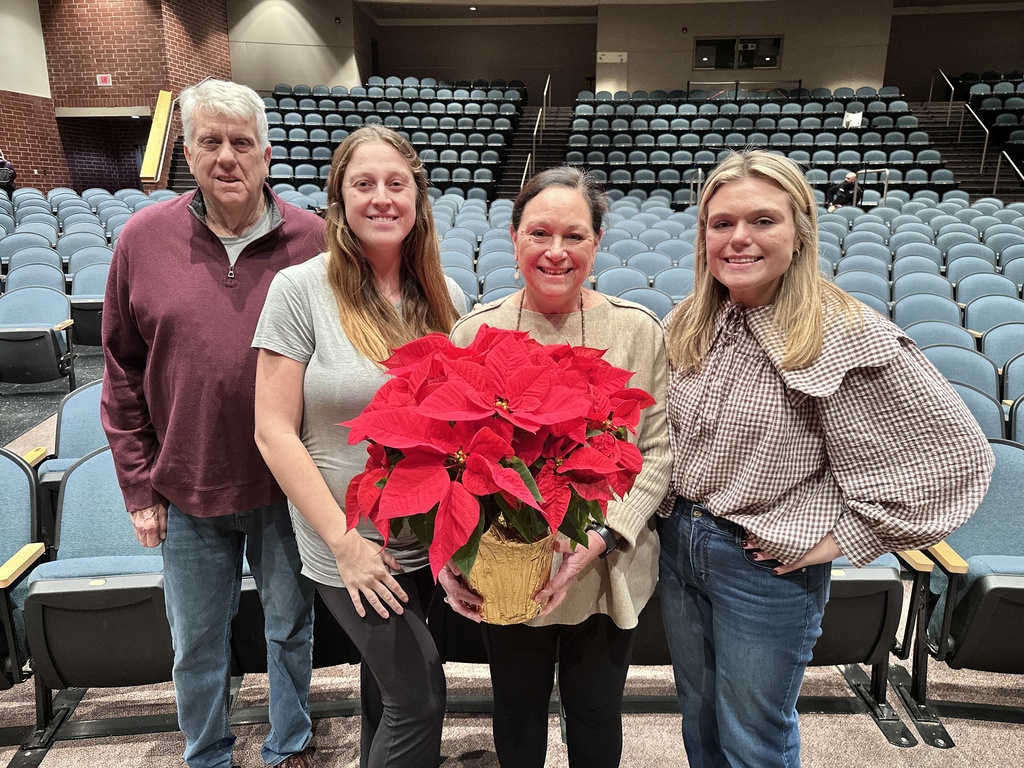 A group of one man and three women pose for a photo in an auditorium.
