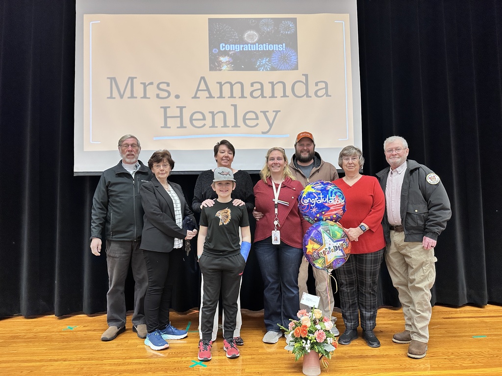 A group of women and men and one child pose for a photo. A slide behind them reads COngratulations Mrs. Amanda Henley.