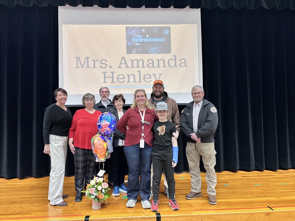 A group of women and men and one child pose for a photo. A slide behind them reads COngratulations Mrs. Amanda Henley.