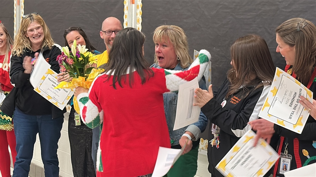 A surprised woman is hugged by another woman while people around her cheer.