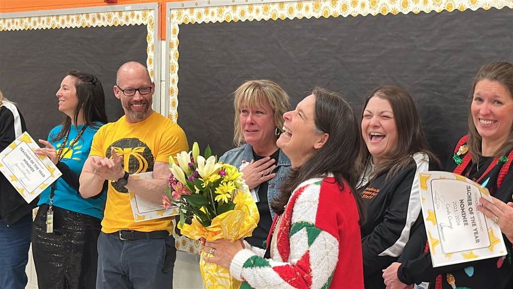 A surprised woman is hugged by another woman while people around her cheer and laugh.