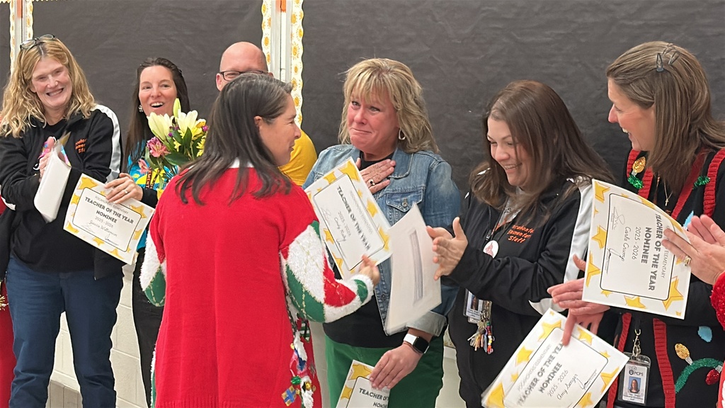 A surprised woman is hugged by another woman while people around her cheer.