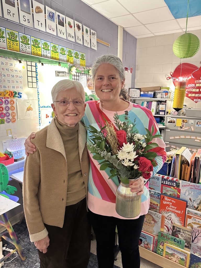 Two women pose for a photo. One holds a certificate and flowers. 