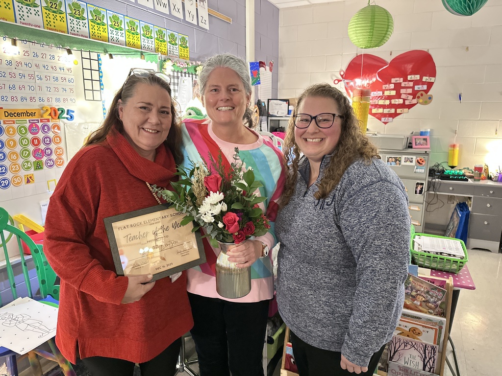 Three women pose for a photo. One holds a certificate and flowers. 
