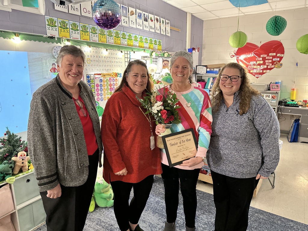 Four women pose for a photo. One holds a certificate and flowers. 