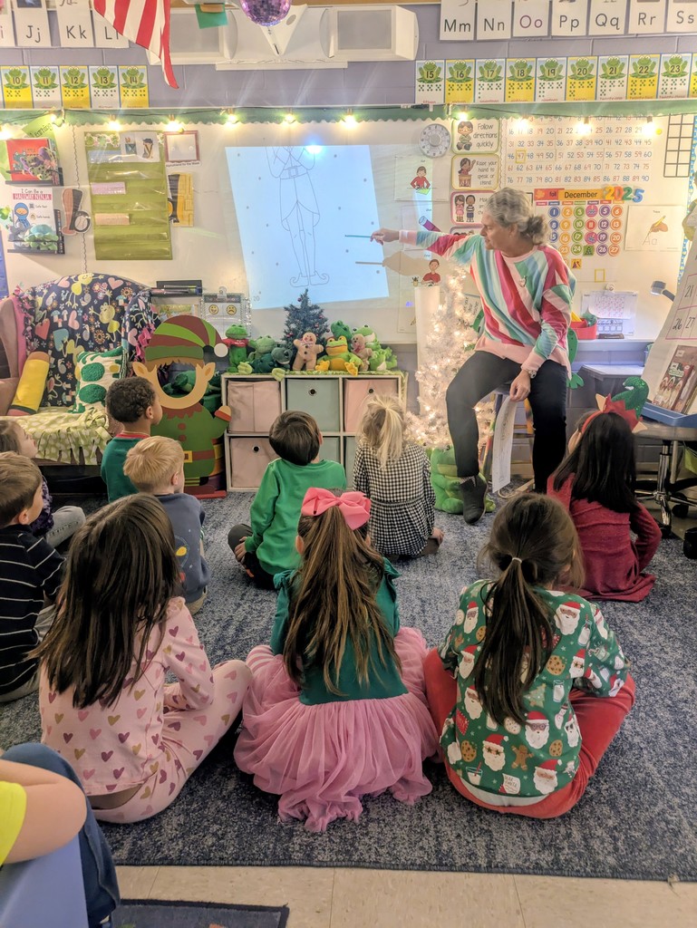 A teacher at the front of a classroom teaches students sitting in front of her.