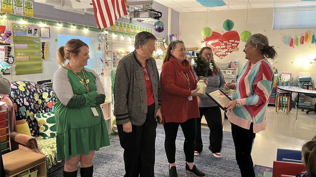 A woman is surprised by a group honoring her as a school-level teacher of the year. 