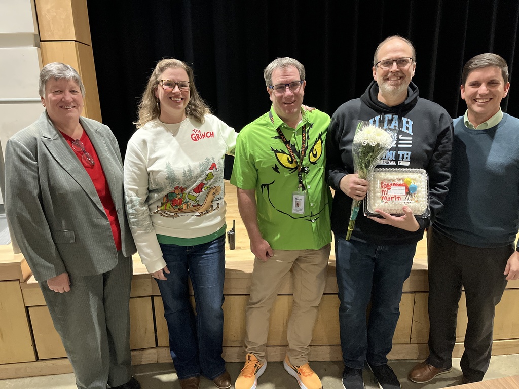 A group of men and women pose for a photo.  One man has flowers and a cake.