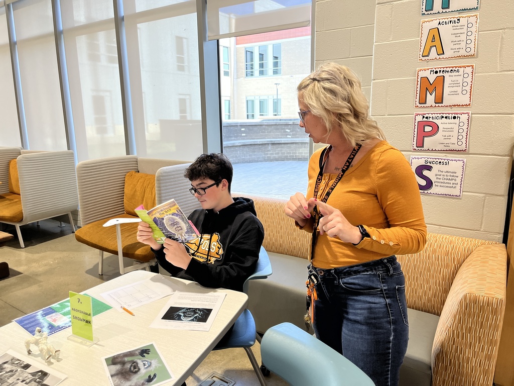 A student participates in a Mysteries, Myths, and Monsters research unit  in the library. A teacher helps.