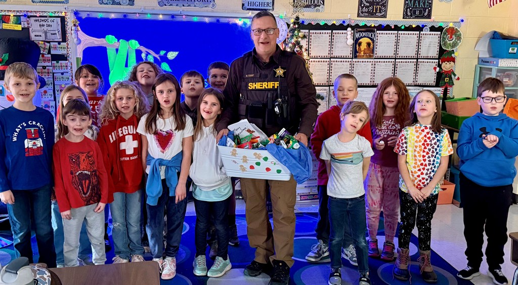 A deputy holds a gift basket given to him by a group of students posing with him.